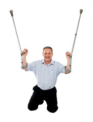 Image showing Cheerful senior man holding crutches upwards