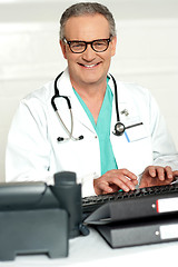 Image showing Smiling physician in eye wear typing on keyboard