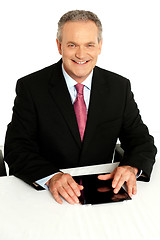 Image showing Senior businessman sitting with tablet on desk