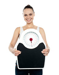 Image showing Cheerful young woman holding a weighing