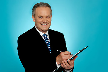 Image showing Attractive senior man writing on clipboard