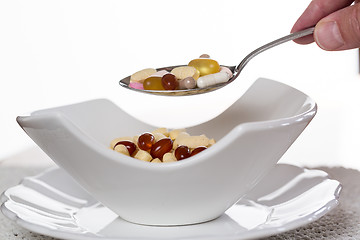 Image showing Spoon of vitamins over bowl of tablets