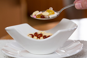 Image showing Spoon of vitamins over bowl of tablets