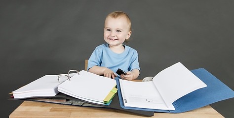 Image showing baby with paperwork at wooden desk