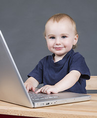 Image showing baby with laptop computer in grey background