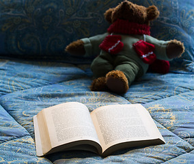 Image showing Paperback book open on bed with teddy bear