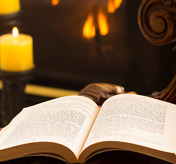 Image showing Paperback book open on chair by fire and candle