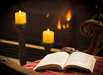 Image showing Paperback book open on chair by fire and candle