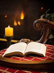 Image showing Paperback book open on chair by fire and candle