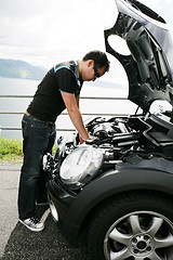 Image showing A young man fixing his car up the hills