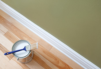 Image showing Paintbrush and an open can of white paint on wooden floor