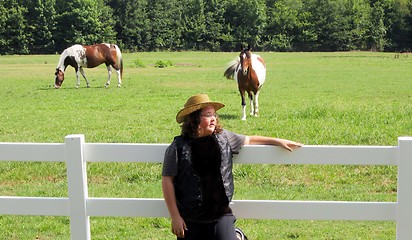 Image showing Young boy leaning on fence wtih two horses in background