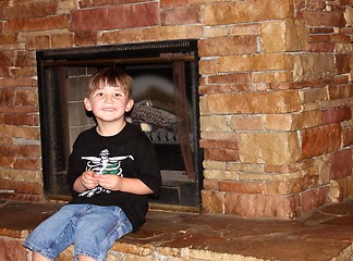 Image showing Cute little boy sitting on fireplace