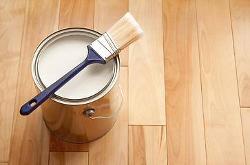 Image showing Paintbrush and a can of white paint on wooden floor