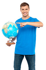 Image showing Casual cool guy pointing at rotating globe