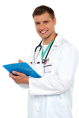 Image showing Smiling young doctor writing on clipboard