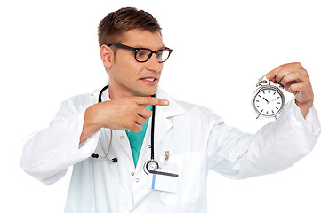 Image showing Shocking young doctor pointing at alarm clock