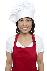 Image showing Young smiling female chef wearing red apron