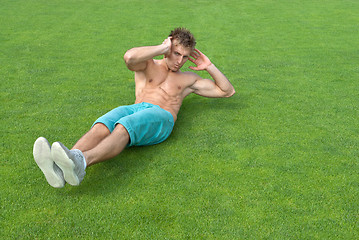 Image showing Young man doing sit-ups on green grass