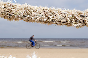 Image showing closeup thick rope and cyclist go sea coast beach 