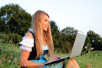 Image showing Bavarian Girl with Laptop in a flowering meadow