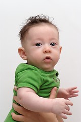 Image showing Cute serious baby held by his mother turns toward the camera