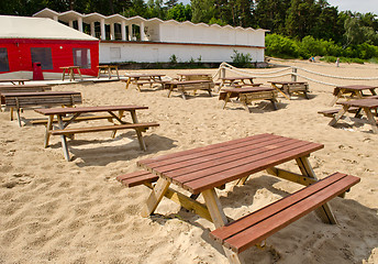 Image showing Wooden tables and benches surrounded by sea sand and huge cafe tent. 