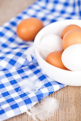 Image showing eggs in a bowl, towel and feathers on rustic wooden table