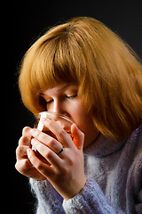 Image showing girl in a sweater on a black background drinking tea