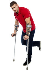 Image showing Painful expression of young guy walking with help of crutches