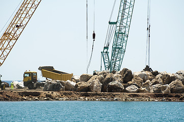 Image showing Building a dike. Cranes and excavator put stones