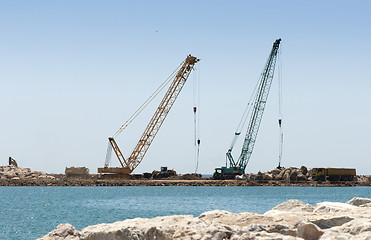 Image showing Building a dike. Cranes and excavator put stones