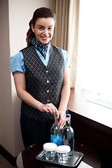 Image showing Cheerful waitress opening bottle of beverage