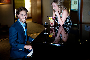 Image showing Man playing piano and entertaining his companion holding cocktail