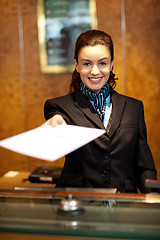 Image showing Cheerful female receptionist offering check-in papers