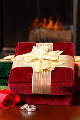 Image showing Wedding rings with Christmas gifts and a rose in front of a fire