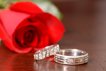 Image showing Two wedding rings with a red rose on a table