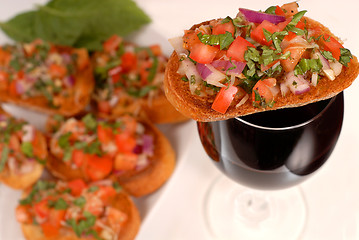 Image showing Bruschetta resting on a glass of wine with additional bruschetta