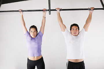 Image showing Female and male bodybuilder doing pull-ups on metal bar on gym