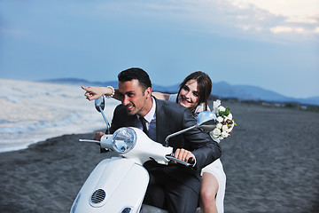 Image showing just married couple on the beach ride white scooter