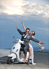 Image showing just married couple on the beach ride white scooter