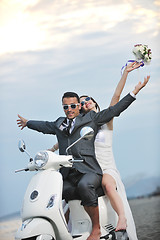 Image showing just married couple on the beach ride white scooter