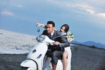 Image showing just married couple on the beach ride white scooter