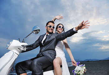 Image showing just married couple on the beach ride white scooter