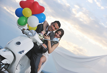 Image showing just married couple on the beach ride white scooter