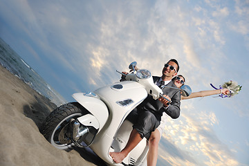 Image showing just married couple on the beach ride white scooter