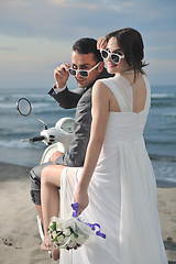 Image showing just married couple on the beach ride white scooter