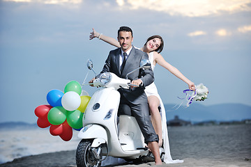 Image showing just married couple on the beach ride white scooter