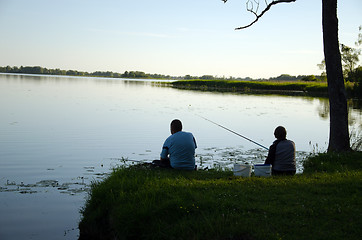 Image showing Man and woman sit on lake shore with rods fishing 