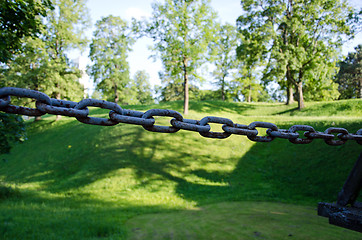 Image showing rusty steel chain and green mound blurred 